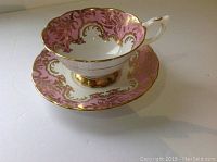Side view of Royal Stafford cup on matching saucer showing pink and gold ornate pattern and gold base on cup.