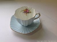 View of cup on saucer showing floral interior and scalloped edges with gold trim