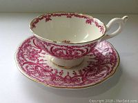 Side view showing ornate pink floral pattern on white porcelain cup and matching saucer with gold trim.