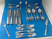 Full view of set arranged on blue background showing all items included: knives, spoons, forks and teaspoons.