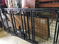 Full view of black metal single bed frame with grid support and attached electronic components in ambient storage area.