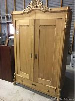 Full front view of solid wood armoire cabinet showing carved top, doors and drawer