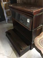 Wooden display case viewed from angle showing top and middle shelf with hinged glass door, surface wear and scratches visible, lower portion detached and lying on floor.
