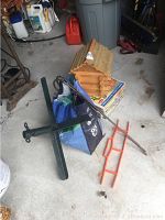 Birdhouse on top of box with black metal base stand and orange hanging basket hooks on concrete floor