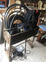 Wicker planter box containing coiled black plastic drainage hoses of various sizes.