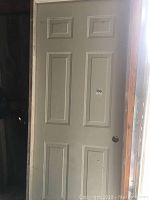 Full view of 6-panel white door with visible scratches and dirt, showing door knob hole, installed or leaning within wooden frame.