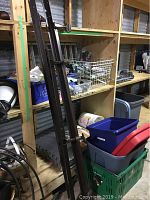 Metal bed frame rails and parts leaning against shelving with assorted household items