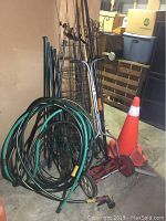 Manual reel lawn mower, garden hoses coiled, wire tomato cages, and safety pylon cone stored in garage.