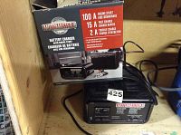 Photo showing the Motomaster battery charger unit with its box on top, displaying brand and charging specs (100A engine start, 15A fast charge, 2A trickle charge).