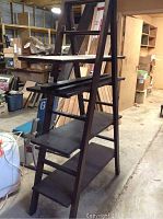 Angled front-side view showing four dark wood shelves supported on a ladder frame in a workshop environment.