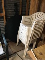 Stacked 12 white plastic chairs showing slight wear and scratches on legs.