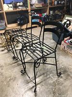Three black metal bar stools with scroll detail viewed side by side in storage area.