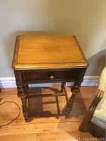 Front view of wooden table showing rectangular top, single drawer with knob, turned legs, and base supports.