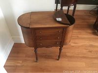 Front view of closed wooden sewing table showing oval hinged lids and 4 drawers