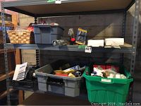View of metal shelving unit with multiple plastic bins containing various home maintenance supplies, including a Rona orbital sander with instructions on the left, and assorted painting tools and accessories in bins.