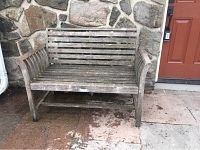 Front view of weathered teak bench showing slatted back, seat and armrests.