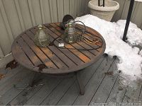 Round metal patio table with two ribbed glass wasp catchers and outdoor lamp on top, showing rust and wear