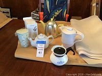 Photo showing the collection of teapots and accessories arranged on table, including ceramic and metal teapots, a measuring container, and boxed tea infuser.