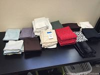 Wide shot of multiple folded pillowcases in different colors and sizes laid out on a black surface.