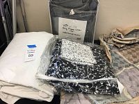 Black and white floral blanket folded in clear plastic and gray folded duvet cover in plastic with product label.