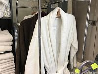 Four bamboo bathrobes hanging on rack, includes three brown and one white robe.