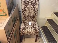 Front view of the brown and cream patterned side chair with wooden legs, placed near packed cardboard boxes.