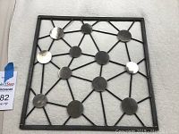 Top-down view of black metal abstract wall art with circular metal discs connected by lines inside square frame.