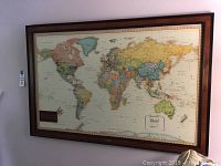 Full view of large magnetic world map framed and hanging on wall, showing North and South America and part of Europe and Africa.