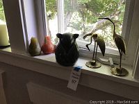 Overview photo of all items displayed on a window sill with natural light showing two metal birds, the ceramic ram, and three shaped candles.