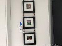 Three black-framed photographs hung vertically connected by decorative links on a light wall.