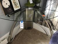 Photo of a corner desk with a glass top and metal base showing curved metal legs and cross supports under a clear glass surface.