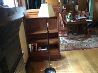 Full view of black metal floor lamp standing next to a wooden bookshelf and a rug visible in the background.