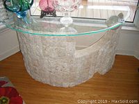 Front-left angled view of the ornate sculptured hall table showing textured base and glass top with decorative items.