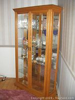 Front and side view of oak finished wooden curio cabinet with glass shelves and mirrored back, doors closed, showing external condition and structure.