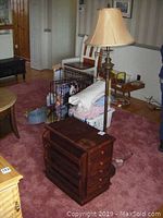 Floor lamp and wooden side table shown together on carpeted floor in living room environment. Lamp is turned off, side table shows a magazine rack on one side and wood finish.