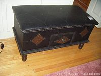 Front view of the black vinyl storage bench showing top cushioned lid and drawer with diamond pattern insets.