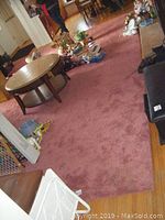 Full view of the dusty rose 12x16 area rug covering a hardwood floor with furniture and household items on it.