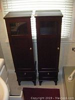 Front view of two matching dark wood tall cabinets with glass panel doors and drawers at the bottom.