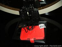 Photo showing Karl Voight binoculars resting on red billfold case with charger cord visible.