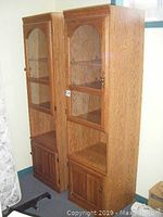Front and side view of the two matching wood display cabinets with glass upper doors and wooden lower cupboard doors.