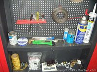 Photo of a shelf inside the Keter tool cabinet showing cans of WD-40, DAP caulking, wire coil, hammer, utility knife, small containers with hardware, and spool of twine.