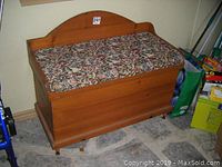 Front angle view of the solid pine blanket box with floral cushion on top showing wood grain and caster wheels.