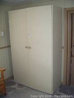 Front view of the beige painted double-door wardrobe with wooden knobs.