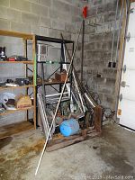Wide view showing scrap metal collected beside shelving unit on concrete floor inside shed.