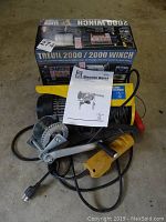 Power Fist electric hoist unit with spool and wired remote, product box and instruction manual visible.