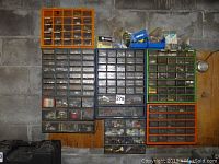 Wide view of five wall-mounted plastic cubbies filled with assorted hardware parts such as nuts, bolts, marettes, springs, and hooks, showing the overall organization and quantity of contents.