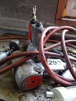 Silver angle grinder with red label and red coiled hoses