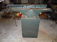 Front view of jointer on pedestal stand showing infeed/outfeed tables and fence with handwheel.