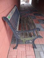 Side angle showing wood slats on seat and back along with ornamental black metal frame and armrests on the bench.
