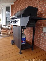 Side view of the black Master Forge gas grill on wheels showing three burner control knobs and attached propane tank below.